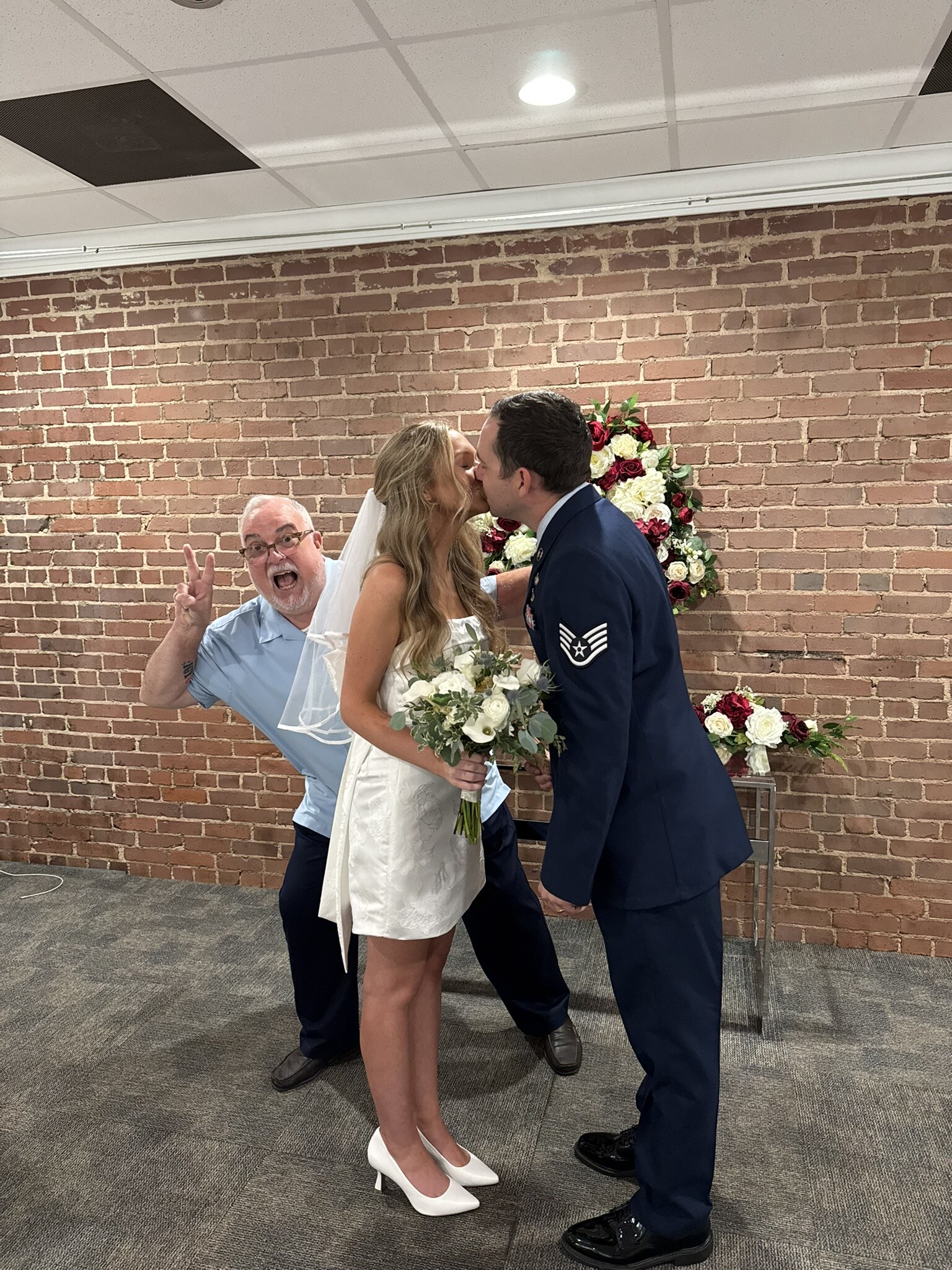 A newly married couple sharing a kiss while Doug celebrates behind them